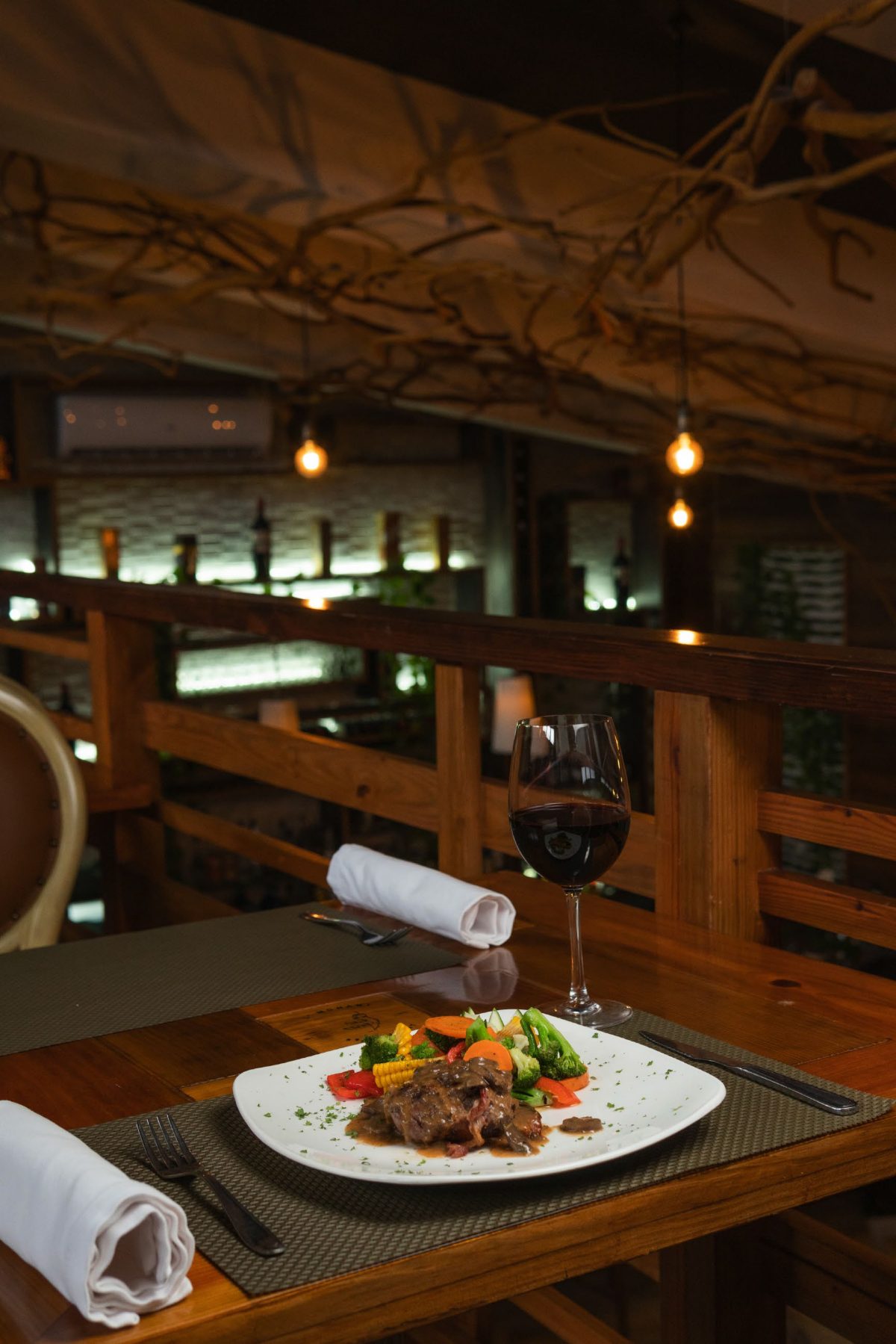 Mesa de restaurante con copa de vino y plato de carne.